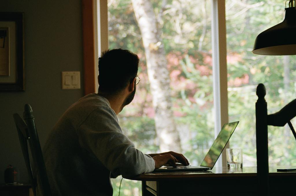 Man sits at a computer, gazing out the window. 