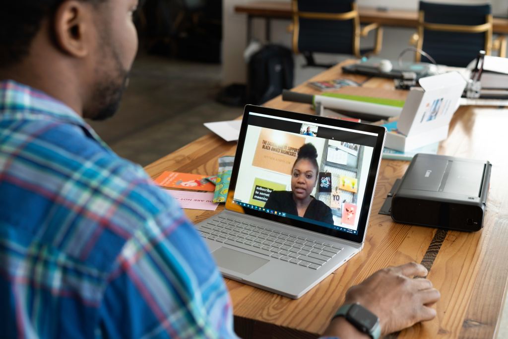 A person sits at their laptop and communicates with someone via video conferencing. 