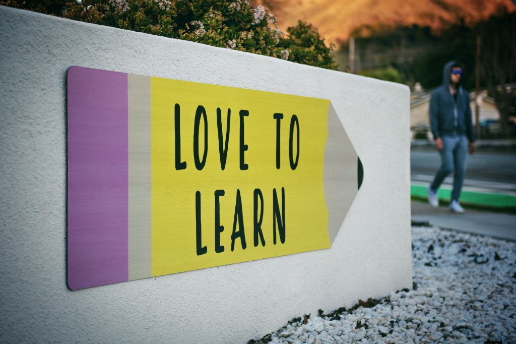 A large outdoor sign with the words "Love to Learn" written on an image of a pencil. 