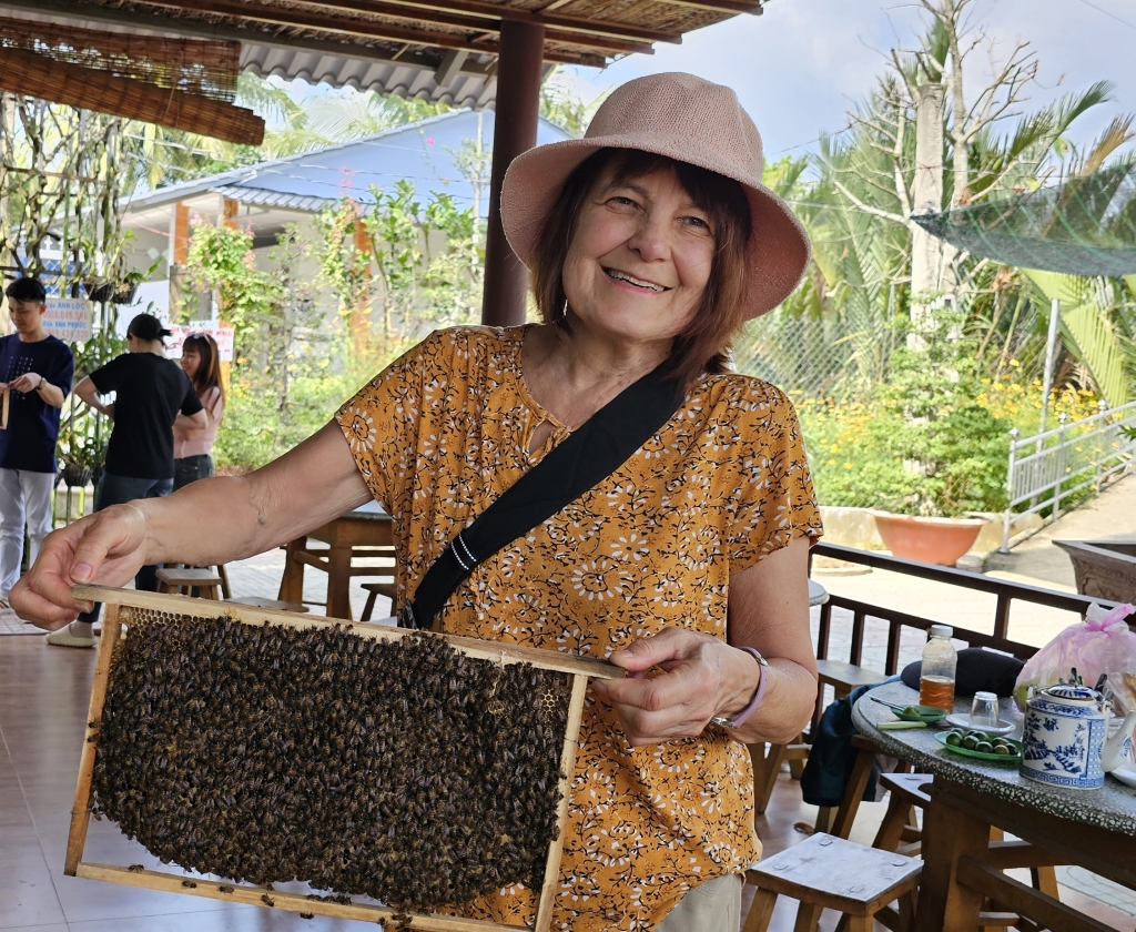 Elizabeth Rains, holding a rack of bees with lush greenery in the background. 